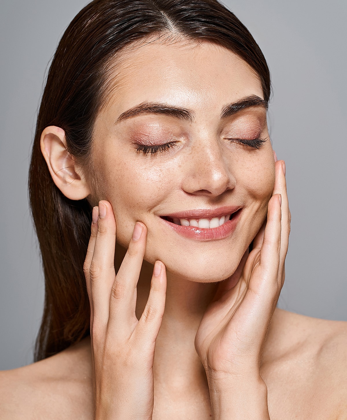 Smiling woman touching her face with closed eyes.